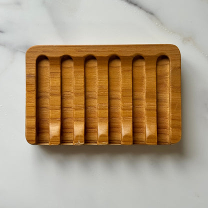 A rectangular wooden tray with six vertical grooves, photographed from above on a light marble surface.