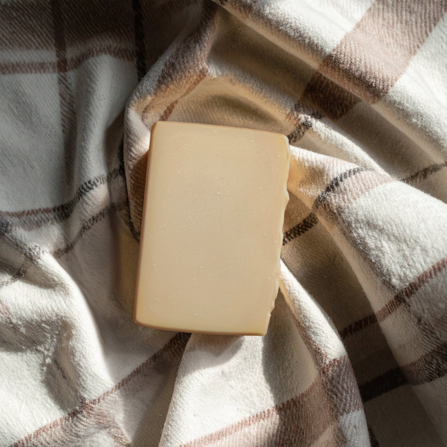 A rectangular bar of creamy beige soap resting on a wooden soap dish filled with lather and foam, set on a white marble surface.