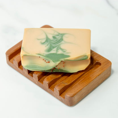 Bar of soap with green swirls on a wooden soap dish against a white background
